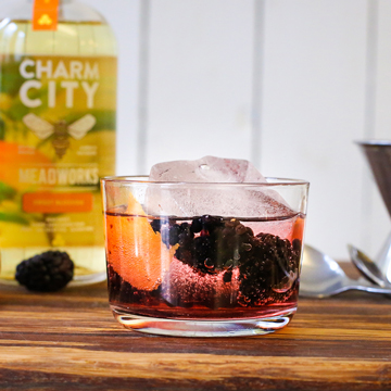 Photo of a bubbly cocktail with a bottle of mead in the background