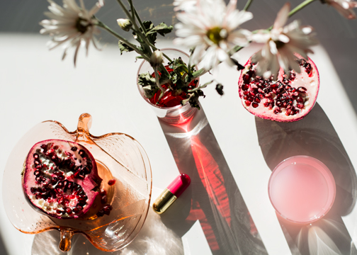 Pink glass reflecting across a table with daisies and pomegranate in the shot