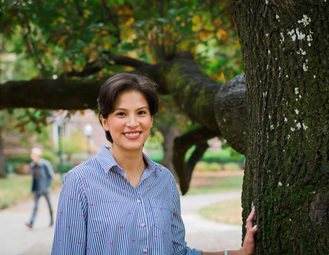Photo of a woman smiling with hand resting on a large tree